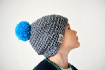 Little boy portrait wearing a grey and blue hat with pom pom.