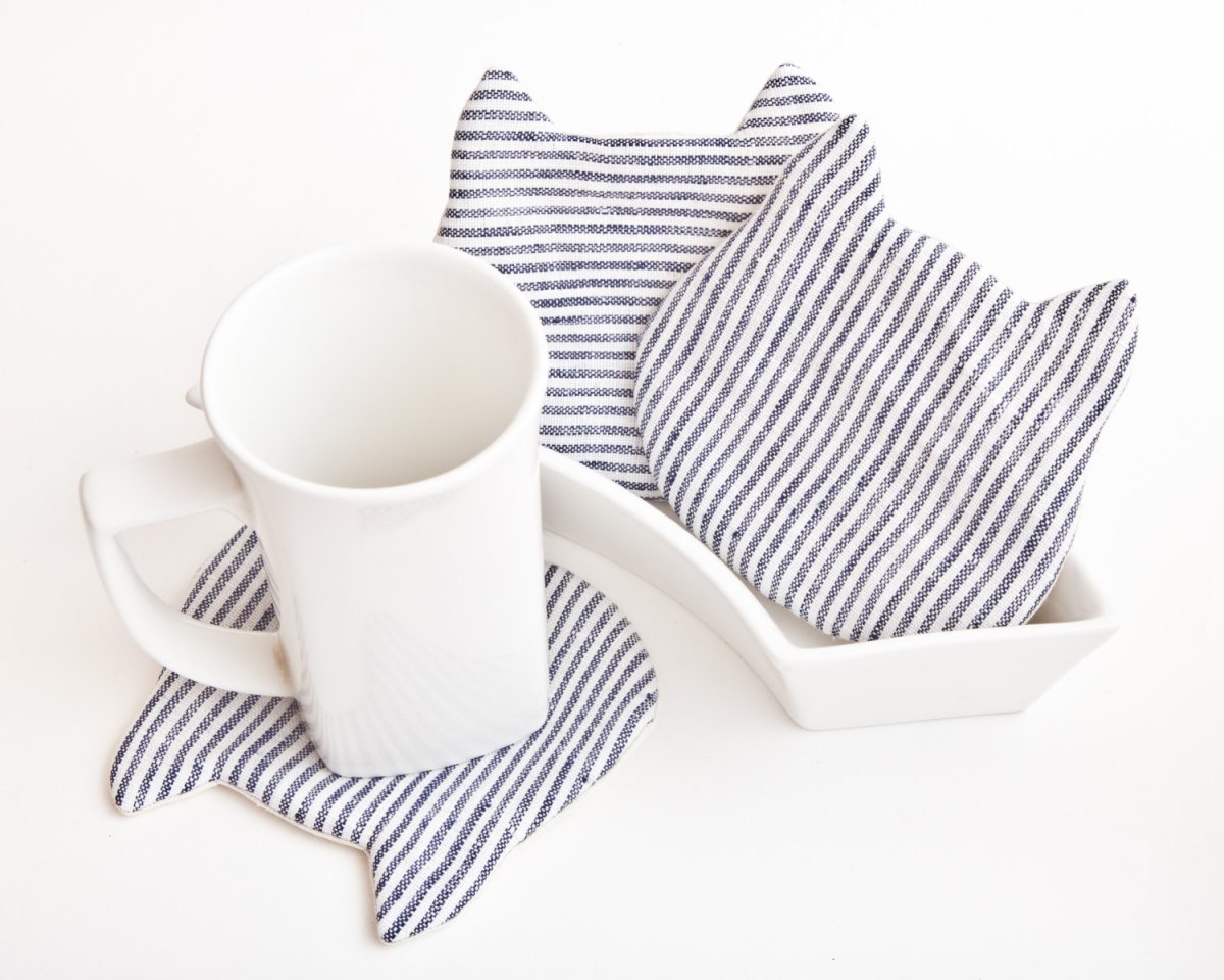 Still life photo of 3 cat shaped cup coasters striped, with a white mug.