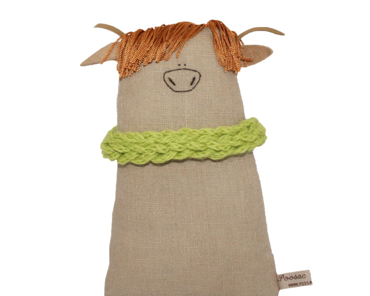 Still life photo of a cow soft toy wearing a green scarf.