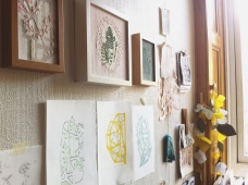 Still live picture of a group of art prints and framed textile artworks on a wall.