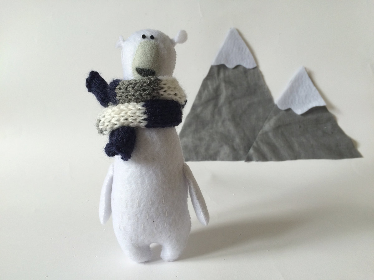 Still life photo of a Felt Polar Bear With Scarf, in the background there are two icebergs made with felt.
