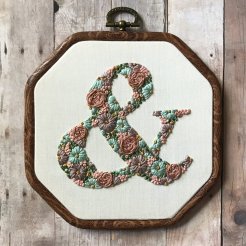 Still life photo of an hand embroidered ampersand on textile surface.