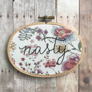 Still life photo of an hand embroidered "nasty" word over a floral textile.